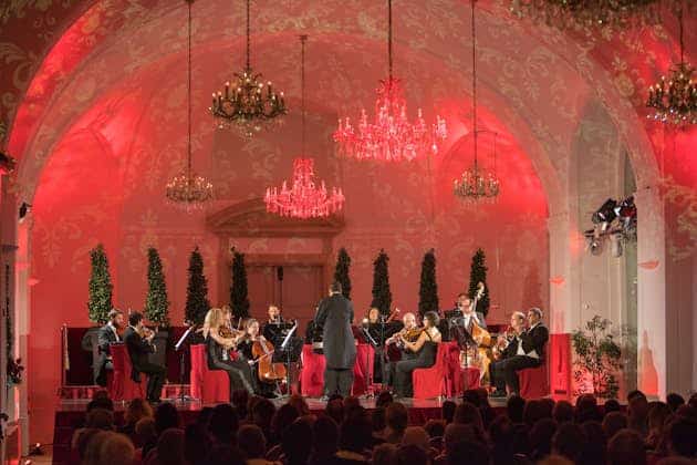 Orchestra performing in elegant, red-lit concert hall.